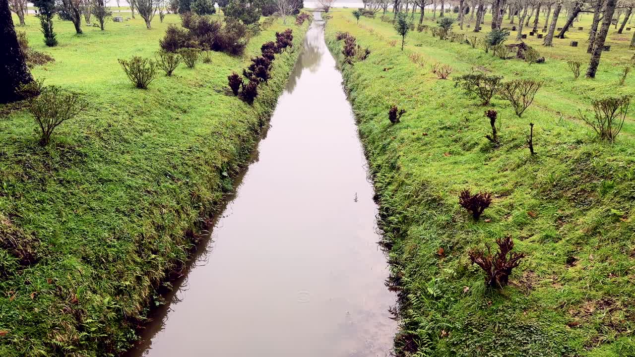 Canale d'acqua rettilineo tra sponde erbose con alberi, São Miguel