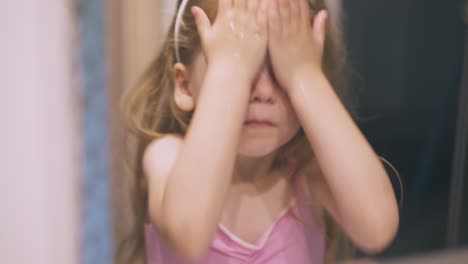 little girl washes face with water at mirror in bathroom