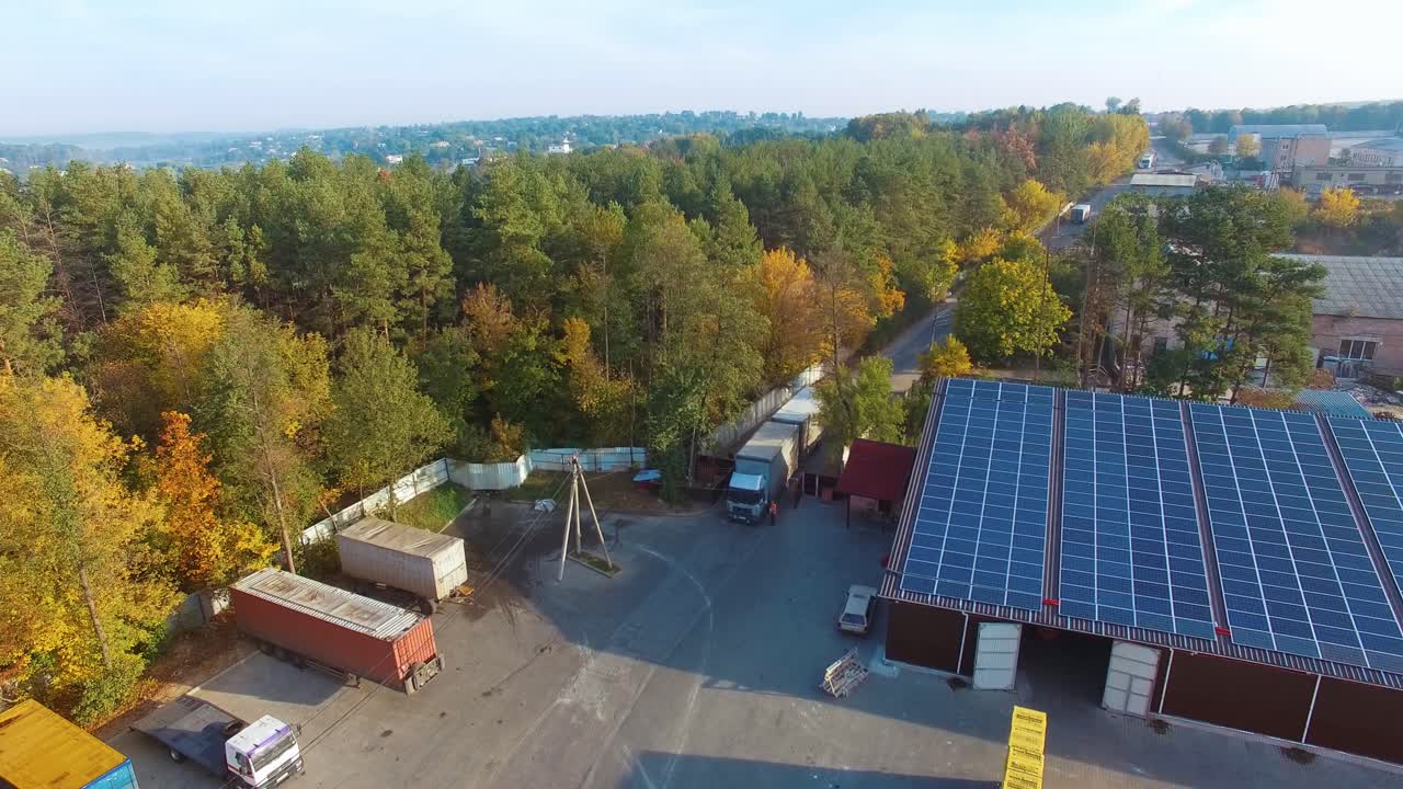 View from above on the road with trucks near green park. Building with solar energy panels in the countryside. Aerial view.