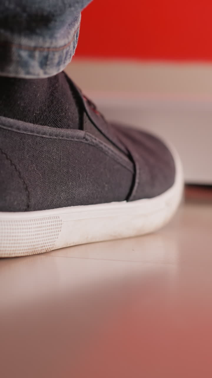 un pie con un zapato negro y pantalones vaqueros azules tocando suavemente un suelo liso y reflectante. el fondo presenta un suave tono rojo, añadiendo calidez y contraste a la escena