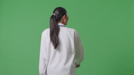 back view of asian female doctor with stethoscope looking around and walking on green screen background in the hospital