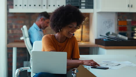 Junge-Lächelnde-Geschäftsfrau,-Die-Am-Schreibtisch-Im-Büro-Am-Laptop-Arbeitet-Und-Mit-Dem-Mobiltelefon-Spricht