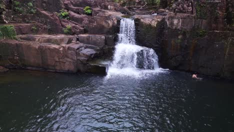 Mann-Schwimmt-Im-See-Vor-Dem-Wasserfall