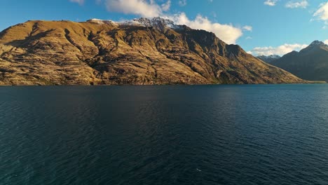 Impresionantes-Rocas-Rojas-Dominan-El-Lago-Wakatipu-Con-Un-Pico-Nevado-Sobre-El-Agua