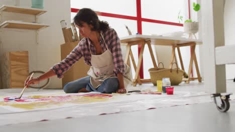 video de una artista femenina biracial pintando en el suelo en un estudio