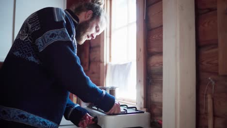 The-Man-Lights-the-Flame-on-the-Stove-and-Begins-Cooking-in-Bessaker,-Trondelag-County,-Norway---Static-Shot