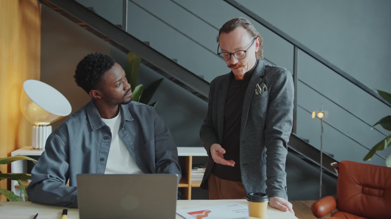 CEO Explaining Male Employee Job Tasks on Laptop in Office