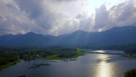 Aerial-Shot-of-Raban-Lake-with-Mountain,-Fish-Farm-and-Forrest-during-beautiful-Sunset-with-God-Ray,-Malaysia