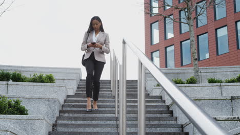 mujer de negocios que viaja al trabajo caminando por las escaleras fuera de la oficina revisando mensajes en el teléfono móvil