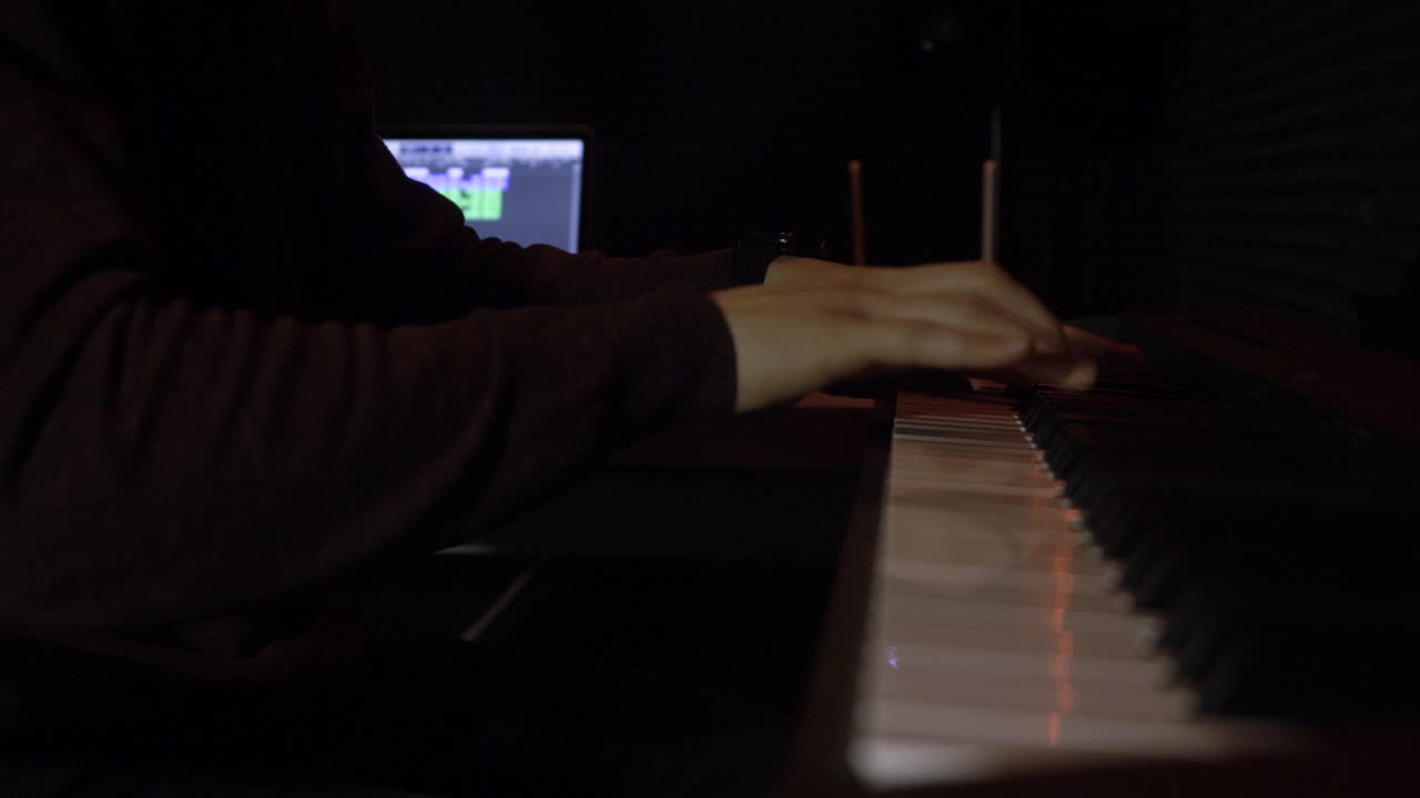 persona tocando el piano en un estudio oscuro