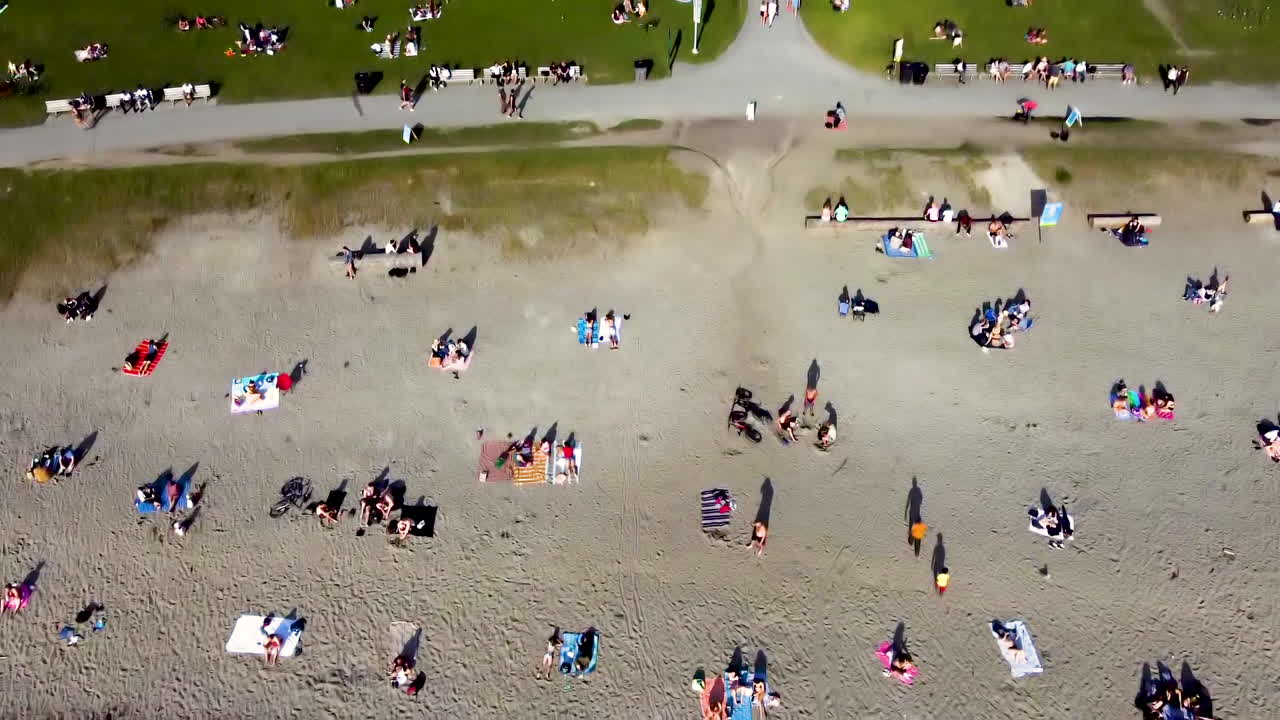 Aerial dolly roll birds eye view over English Bay Harbor during COVID-19 pandemic people are respectful distancing each other physically and socially on hot summer day where its typically over crowded