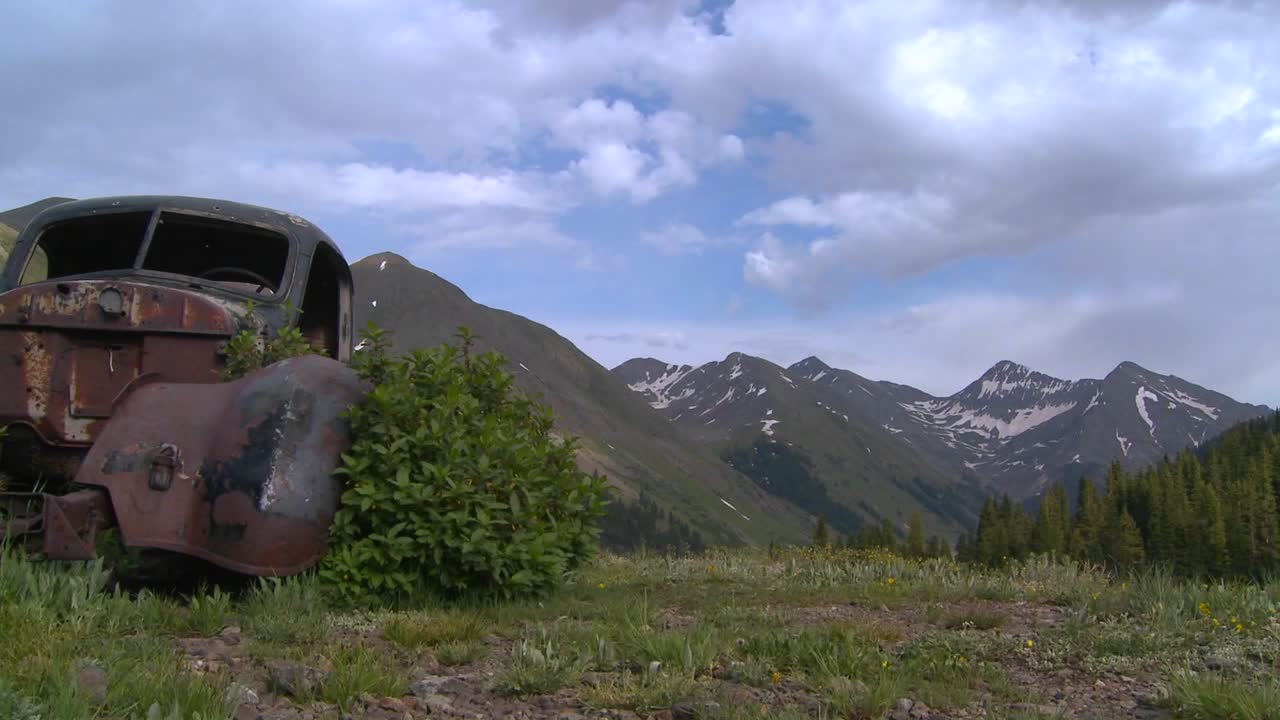 전경에 버려진 오래된 자동차와 함께 록키 산맥을 가로지르는 아름다운 저속 촬영