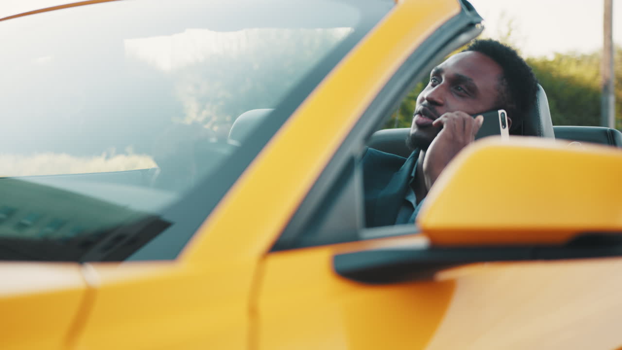 hombre hablando por teléfono mientras conduce un descapotable amarillo