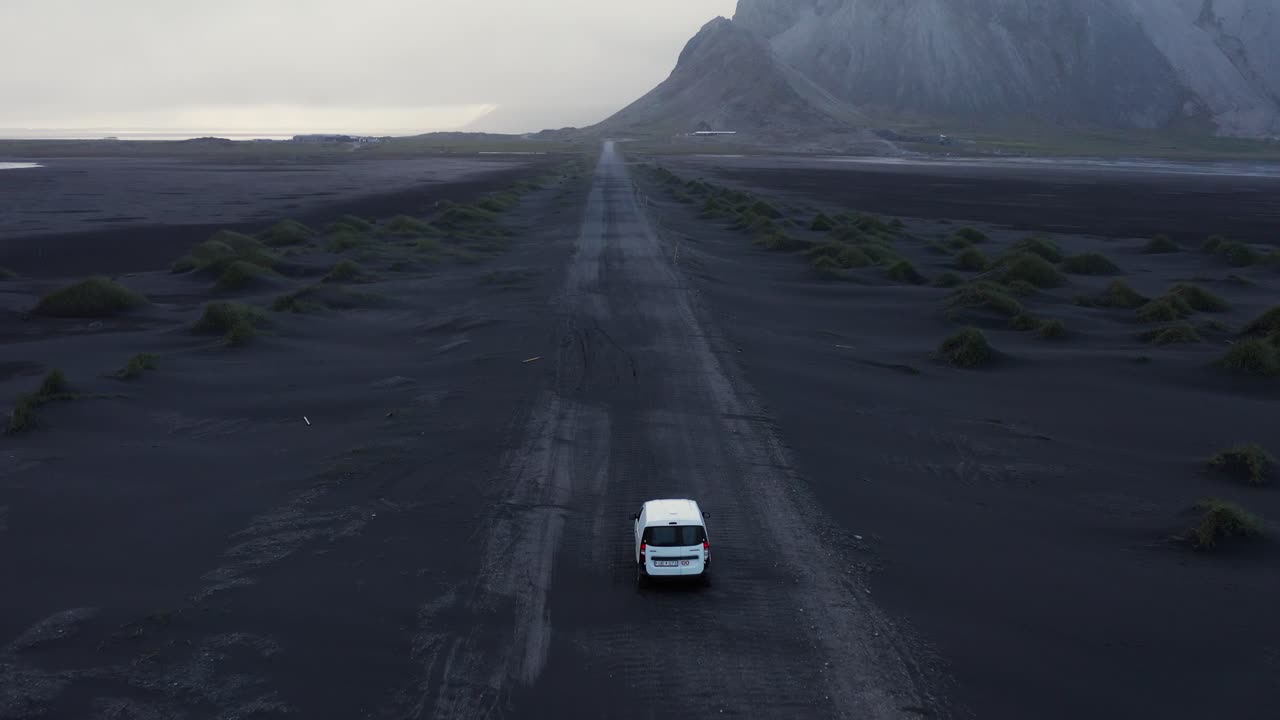 carro branco parado na longa estrada de areia vulcânica preta e reta na islândia, aérea