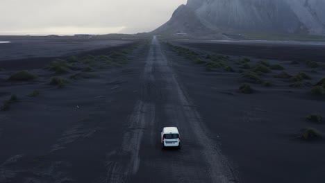 white car standing on long straight black volcanic sand road in iceland, aerial