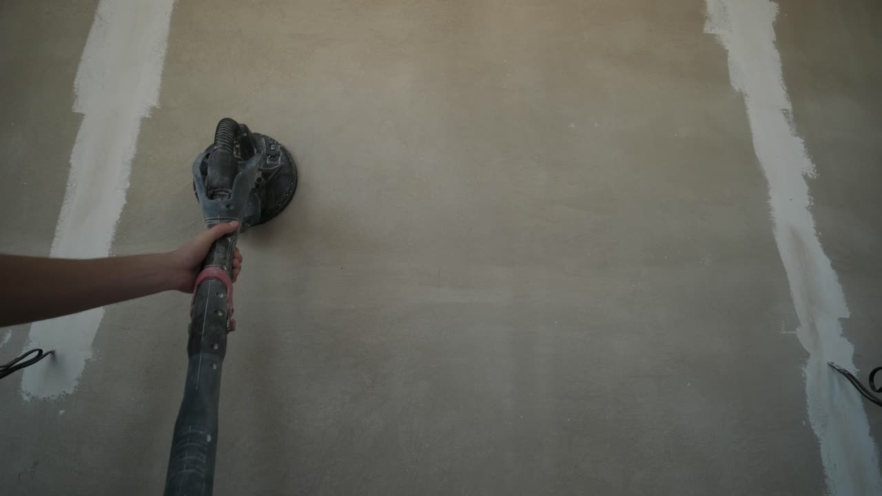Worker using a pole sander to smooth a wall surface during the drywall finishing phase of interior construction