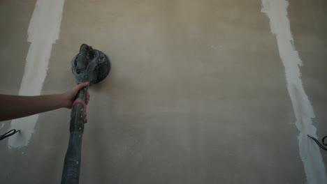 trabajador que utiliza una lijadora de postes para suavizar la superficie de una pared durante la fase de acabado de la pared de yeso de la construcción interior