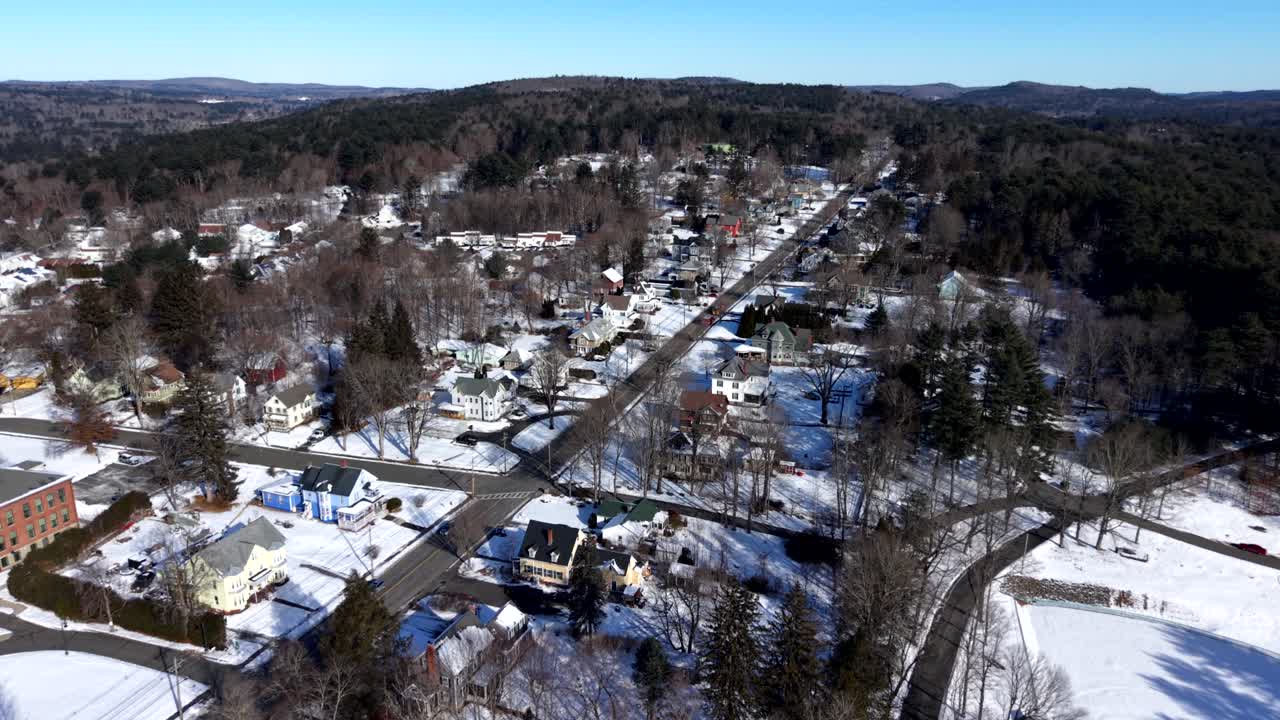 Kışın Ware, Massachusetts'in, açık mavi gökyüzü altında karla kaplı sokaklarını, evlerini ve çevresindeki ormanlık tepelerini gösteren kuş bakışı görüntü. Geniş çekim.