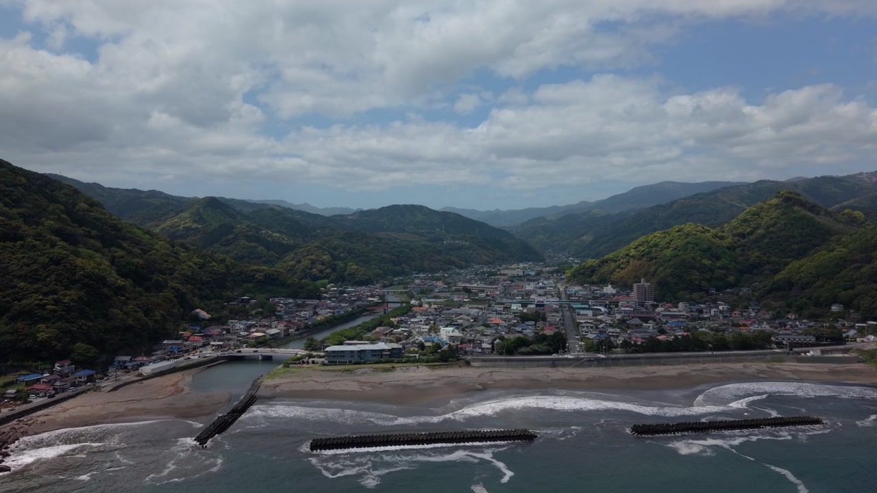 Cittadina costiera alla foce di un fiume sotto montagne boscose a Kawazu, Izu, Giappone, in un pomeriggio fosco, ampia ripresa aerea con drone