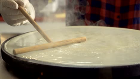 professional cook flatten dough on a hot stove with a wooden spatula