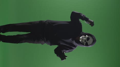 hombre aterrador en la sudadera con capucha con máscara de halloween sosteniendo un cuchillo y haciendo un gesto aterrador mientras camina en el fondo de la pantalla verde