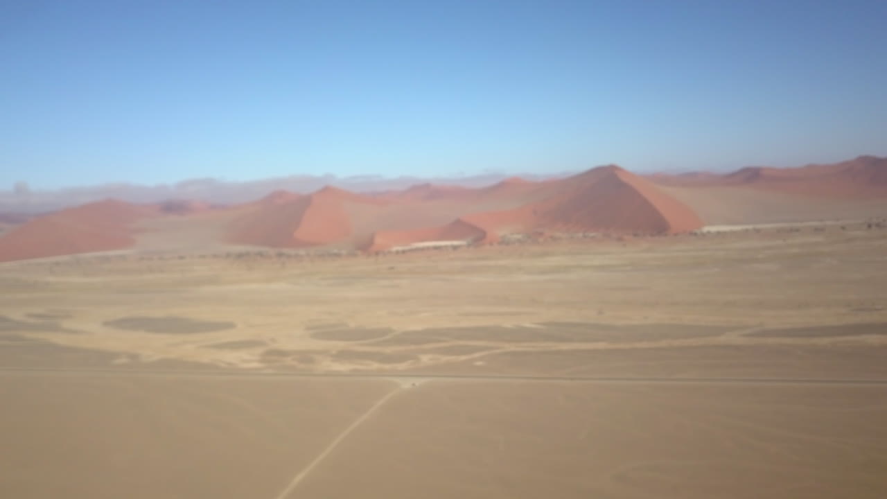 4K aerial drone shot over the iconic red sand dunes of Sossusvlei in Namibia, capturing sweeping desert curves, textures, and surreal beauty in golden light.