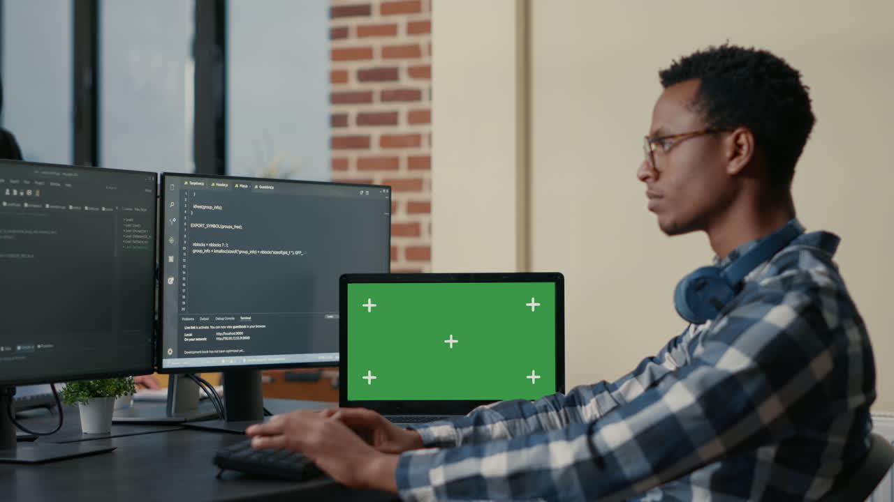 Software developer writing code using computer keyboard and laptop with green screen chroma key mockup