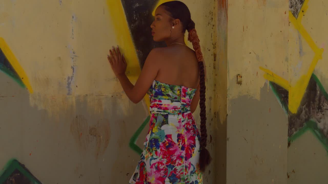 벽에 낙서 옆에 서있는 동안 긴 드레스를 입은 섹시한 소녀가 돌아 서서 주위를 둘러 봅니다.