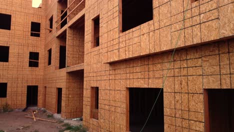 Wood-framed-construction-site-left-abandoned-as-work-stopped-due-to-pandemic-supply-chain-shutdown-drone-flying-up-from-tree-on-ground-to-top-of-4-story-apartment-condo-building