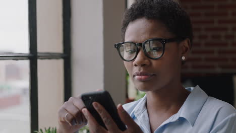 joven mujer de negocios afroamericana que usa un teléfono inteligente en casa navegando por mensajes disfrutando de las redes sociales en línea compartiendo estilo de vida mirando por la ventana enviando mensajes de texto en la tecnología de teléfono móvil usando gafas