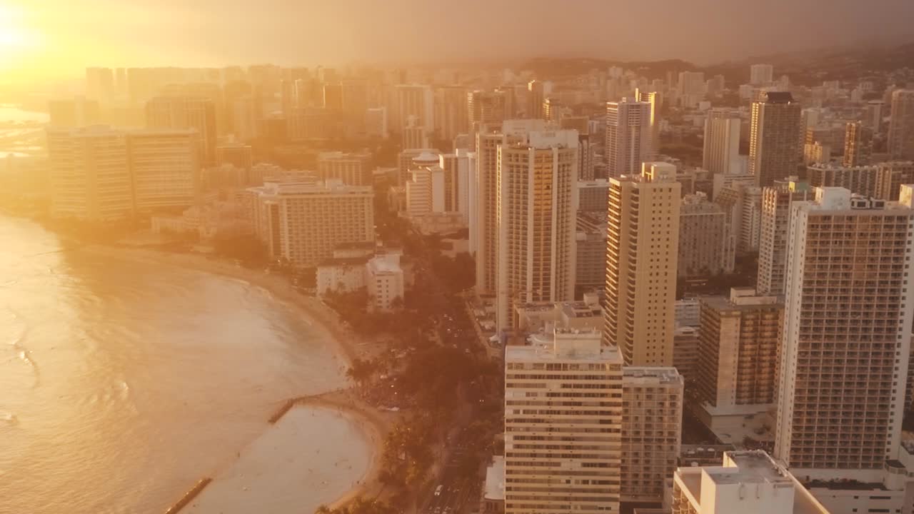 Drone aéreo panorâmico voando lentamente sobre o colorido horizonte de Honolulu durante o pôr do sol em Oahu, Havaí, com a Praia de Waikiki como um ponto de interesse especial