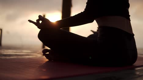 Silhouette-Of-Unrecognizable-Yogi-Girl-Sitting-In-Lotus-Pose-In-Front-The-Sea-Meditating,-Sunshining-Through-The-Hands-On-Knees