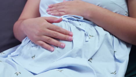 pregnant woman caressing her growing and bulging baby bump while she is sitting on her couch in her living room