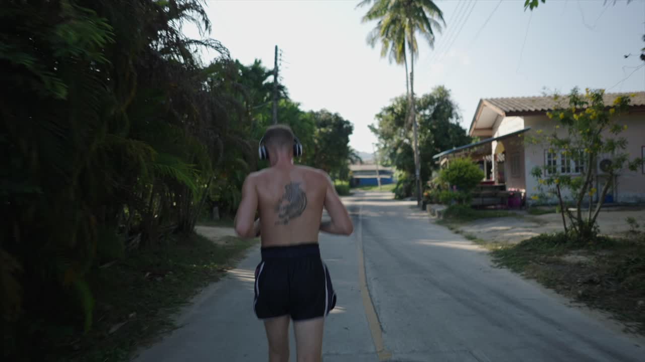 Man with tattoo jogging on a tropical road with headphones