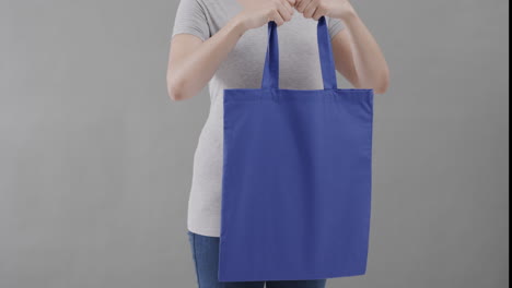 mujer caucásica con camiseta blanca sosteniendo una bolsa azul sobre un fondo gris, espacio de copia, cámara lenta