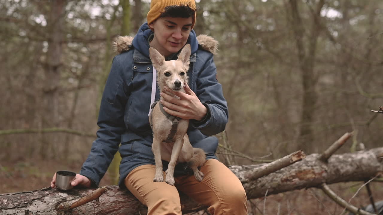 молодая женщина с короткими волосами сидит в лесу и держит маленькую собаку