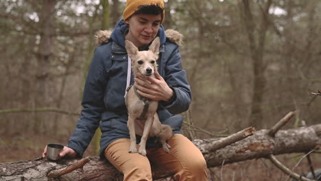 Mujer-Joven-Con-El-Pelo-Corto-Sentada-En-El-Bosque-Sosteniendo-Un-Perro-Pequeño