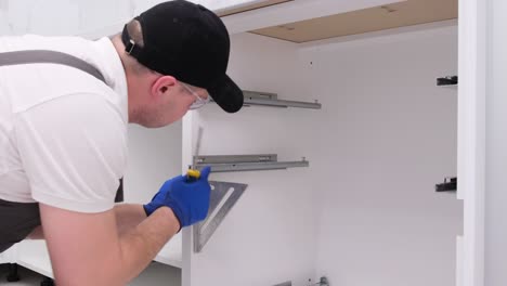 a qualified master in gray overalls installs furniture in a modern bright kitchen a qualified master in gray overalls installs furniture in a modern bright kitchen