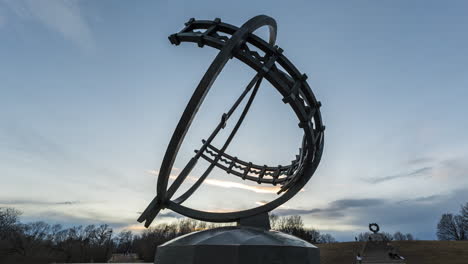 Reloj-De-Sol-De-Bronce-Con-La-Escultura-De-La-Rueda-De-La-Vida-En-El-Fondo-Al-Atardecer-En-El-Parque-Vigeland,-Parque-Frogner,-Oslo,-Noruega