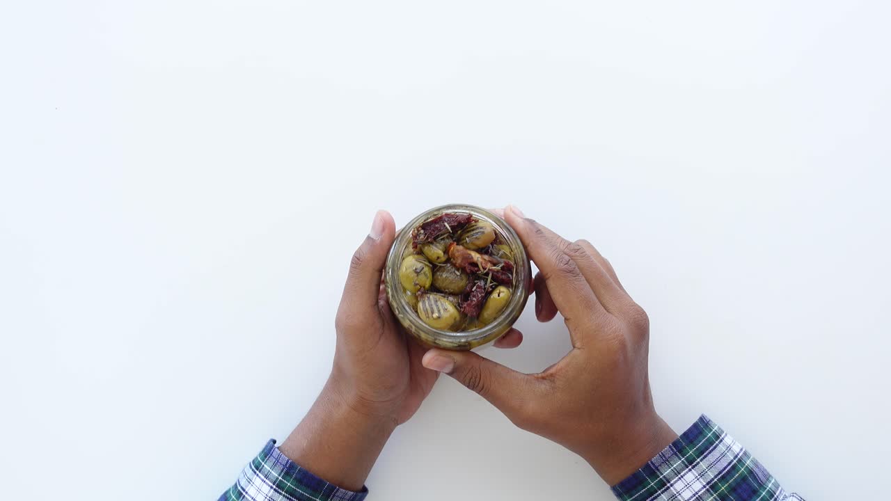 persona que sostiene un frasco de aceitunas verdes y tomates secos al sol