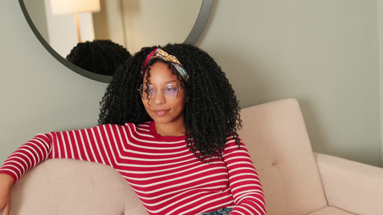 Young Woman with Curly Hair Sitting Thoughtfully on a Couch at Home