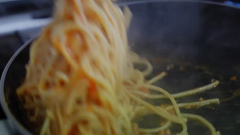 slow motion close-up of tossing spaghetti noodles and bolognese sauce in a frying pan