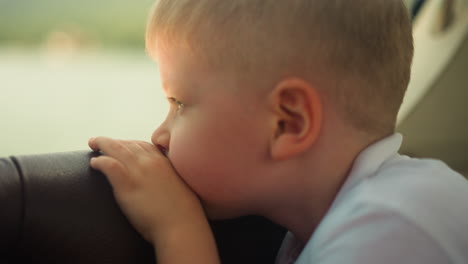 un niño cansado se apoya en la silla mirando por la ventana de una lancha de motor en primer plano. un niño pequeño triste se sienta en una cabina viajando en un barco turístico de vacaciones