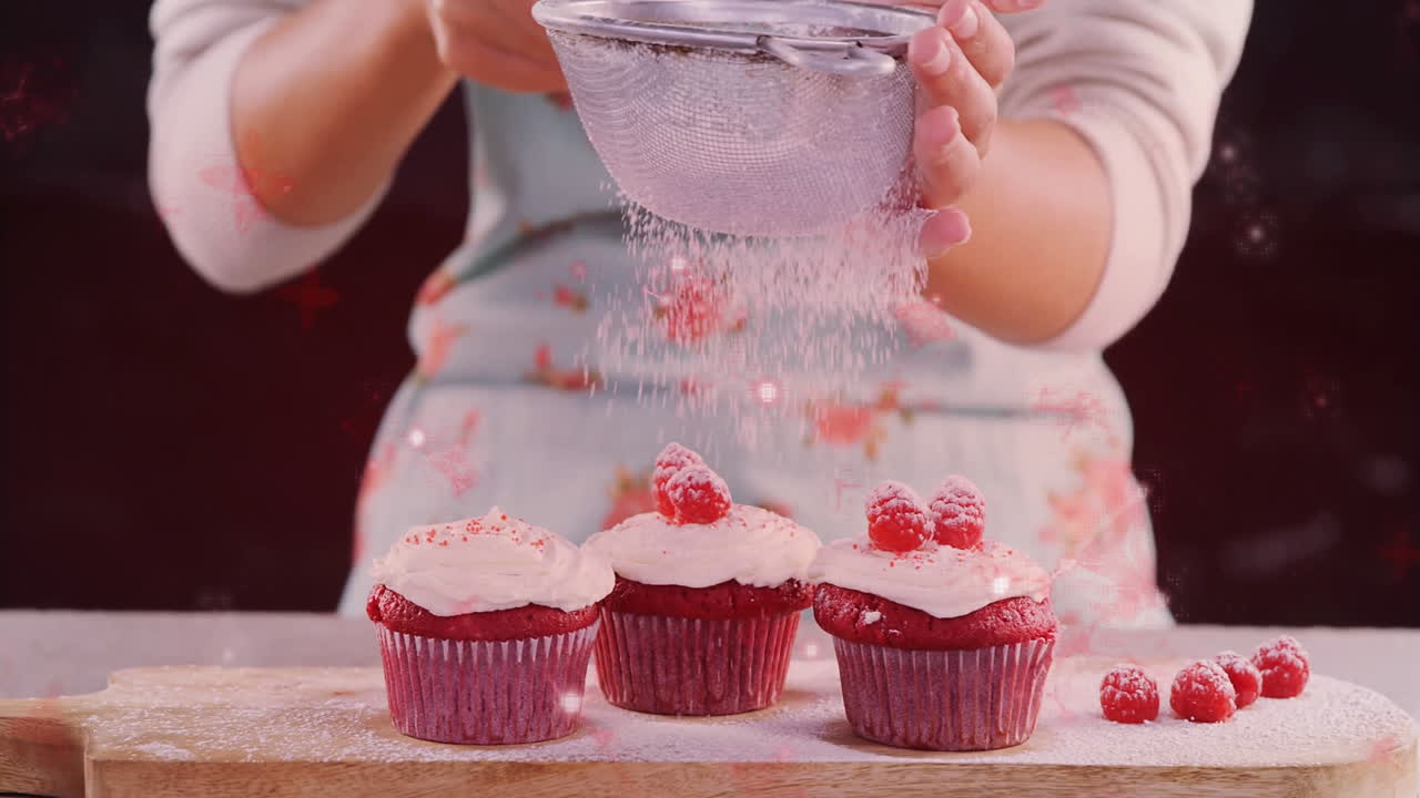 Dusting powdered sugar, baker decorating red velvet cupcakes with raspberries