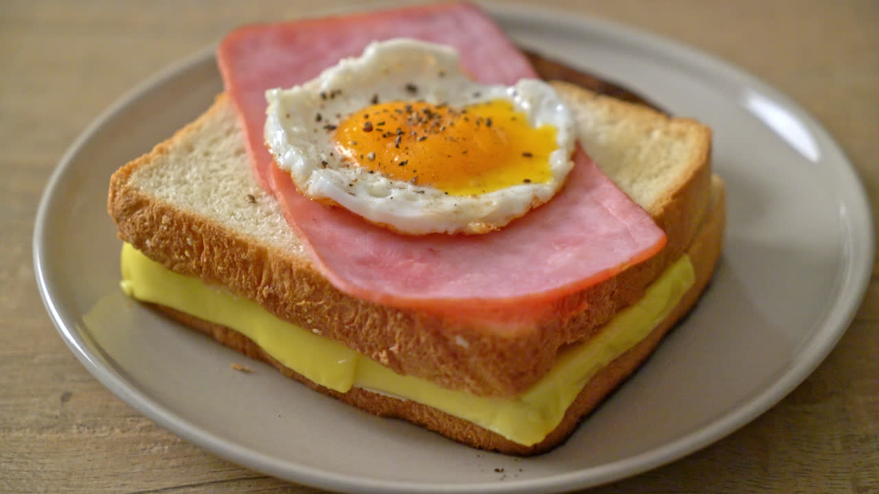 Hjemmelavet brød med ristet ost, toppet med skinke og spejlæg med pølse til morgenmad