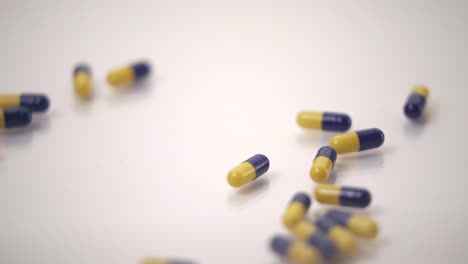 slow motion macro of blue and yellow pills pushing one yellow pill out of frame on white background