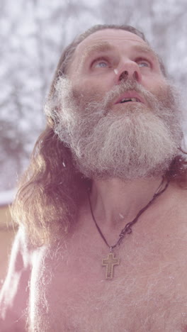 Hippy man bare chested outdoors looking up in snowfall in prayer, vertical