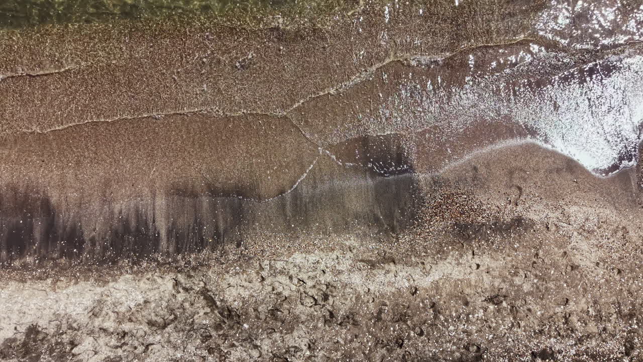 Le onde si infrangono sulla riva sabbiosa durante le ore di luce solare in una località balneare con cieli sereni e acqua calma.
