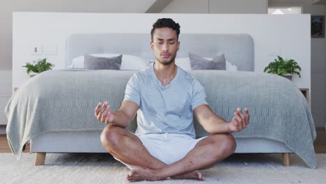 relaxed biracial man sitting on floor in bedroom practicing yoga meditation, slow motion