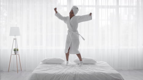 mujer feliz bailando en la cama en bata de baño
